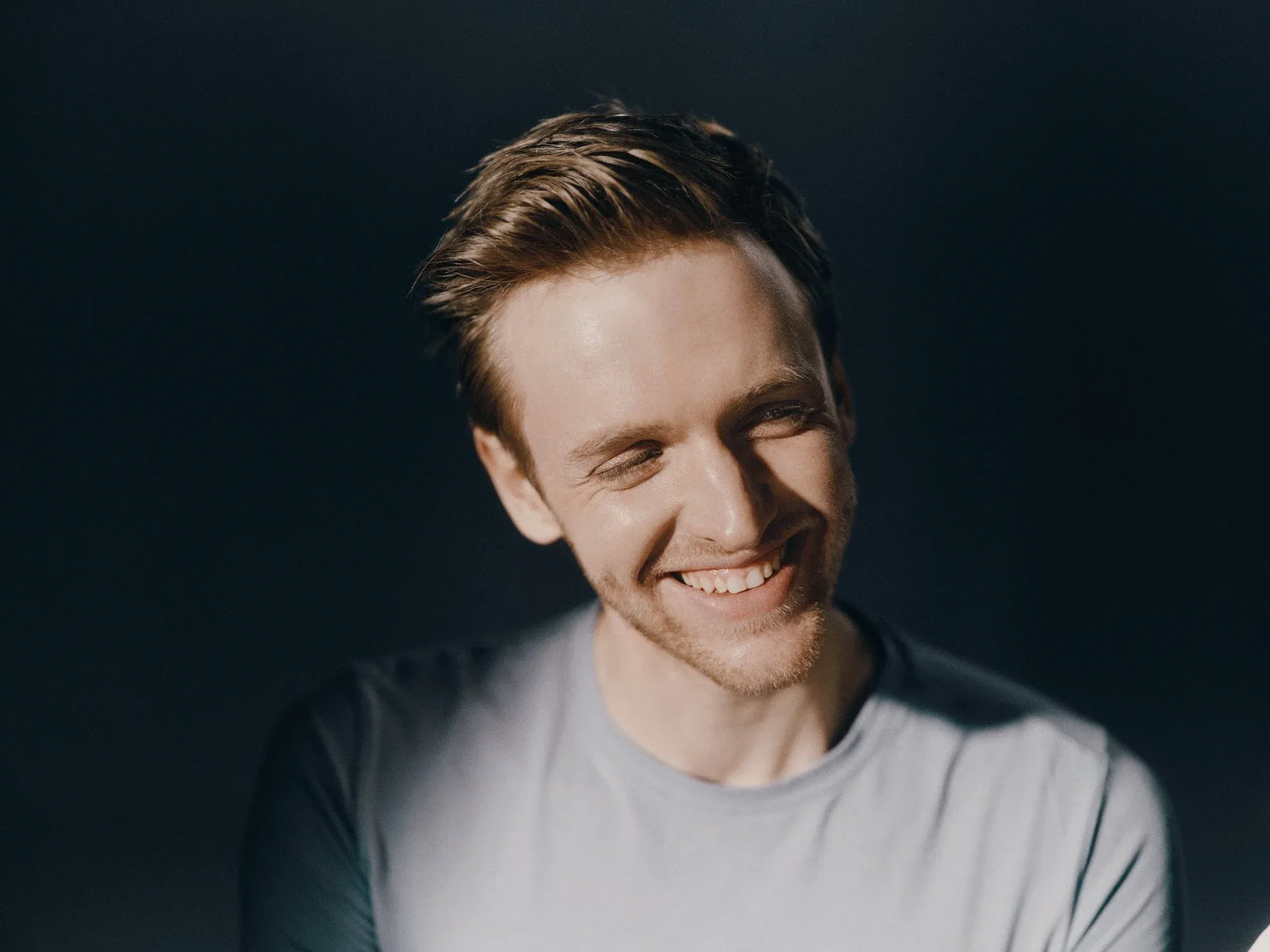 Timur Bartels im grauen T-Shirt vor grauem Hintergrund